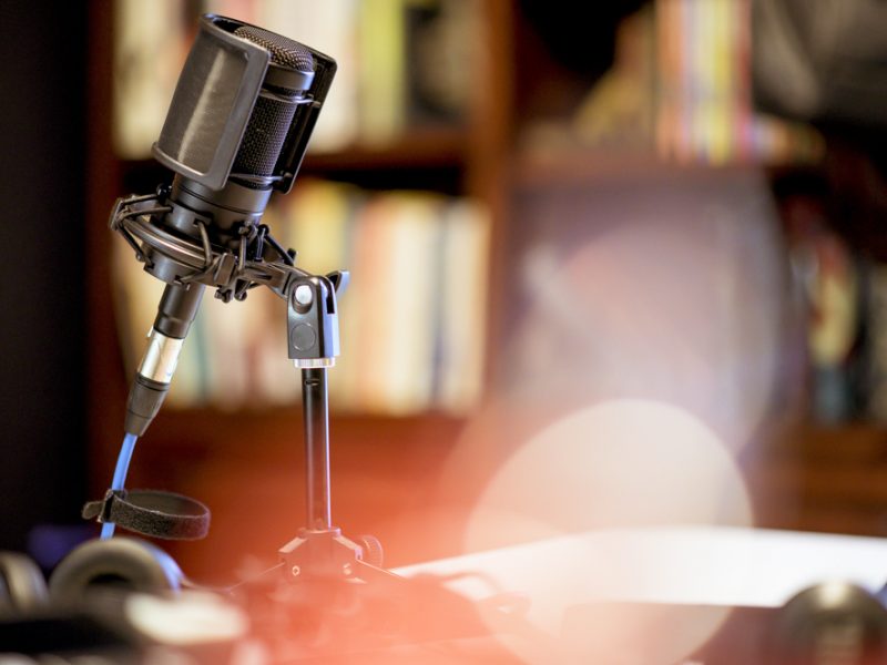 A microphone in a studio surrounded by equipment under the lights with a blurry background